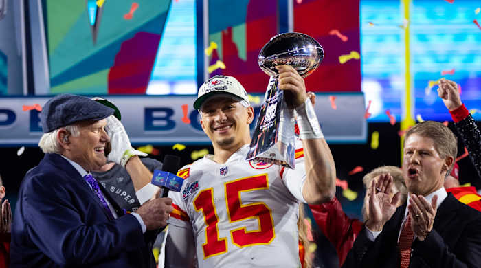 Patrick Mahomes holds up the Lombari trophy in one hand as a man holds a mic toward him and confetti falls